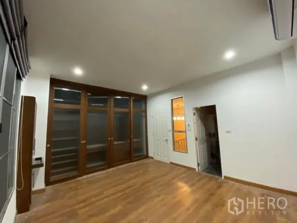 联排别墅 出租在Lat Phrao, Bangkok - 楼上卧室，木地板、内置玻璃柜与筒灯照明。