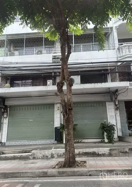 อาคารพาณิชย์ ให้เช่าในBang Na, Bangkok - ด้านหน้าอาคารพาณิชย์ 4 ชั้น ประตูม้วนสีเขียวสองบาน ทางเท้าร่มรื่น ย่านบางนา กรุงเทพฯ