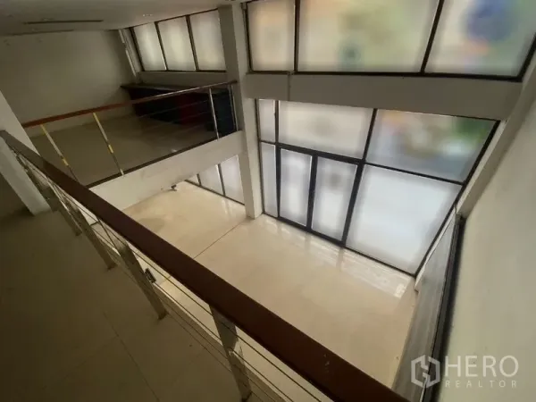 零售空间 出租在Watthana, Bangkok - 室内挑高空间与夹层，金属栏杆，正面为磨砂玻璃落地窗。