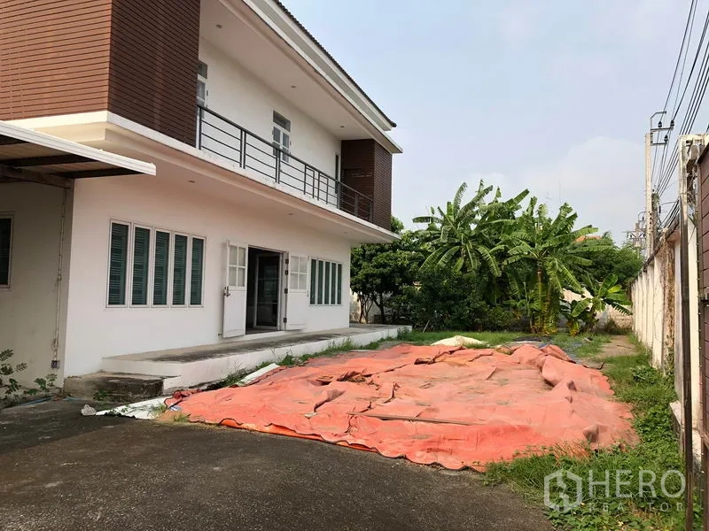 独立式住宅 出售在Bang Khen, Bangkok - 房屋侧视图，长车道与前院空间，围墙旁有香蕉树。