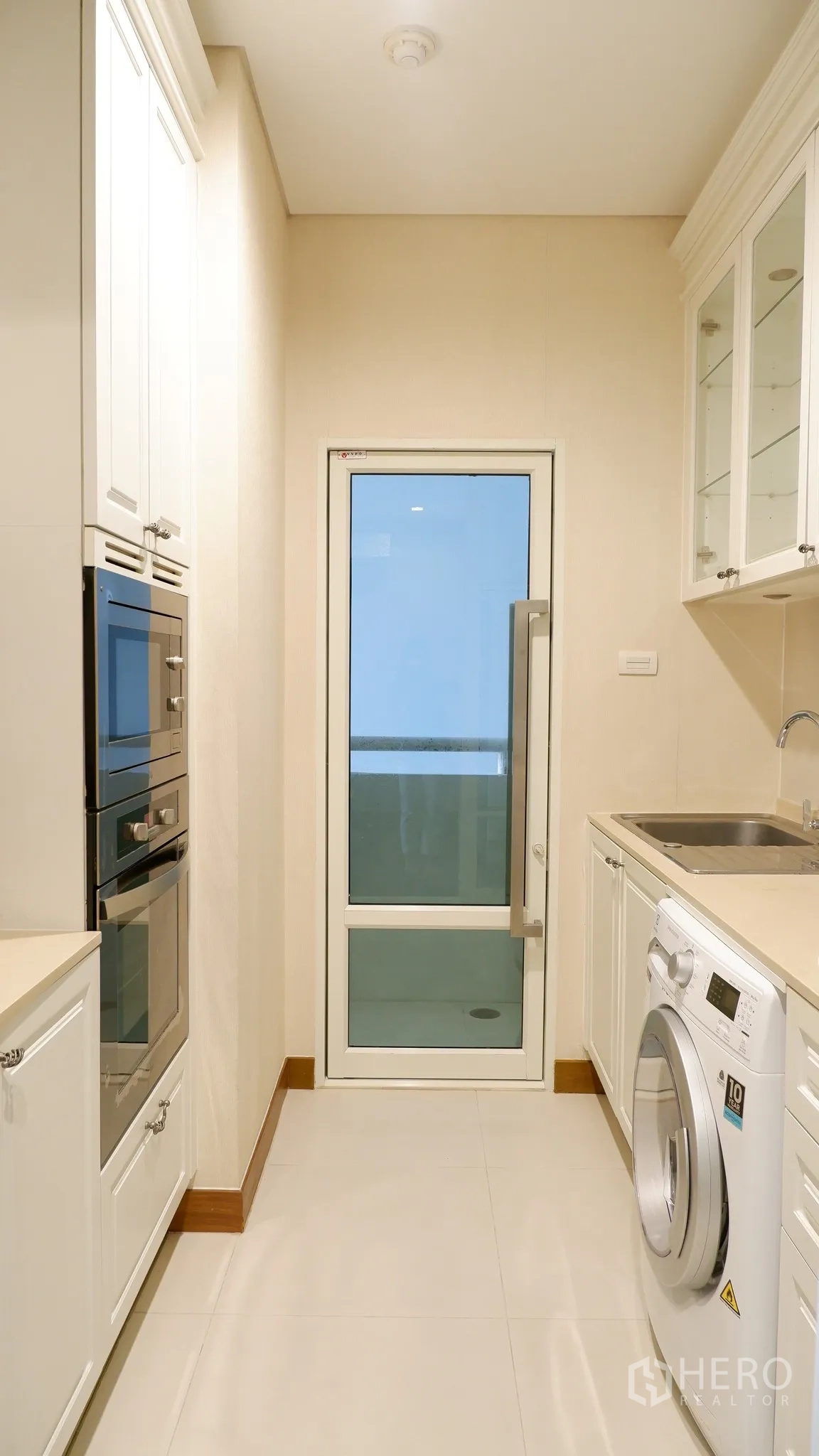 Condominium for rent in Watthana, Bangkok - Galley kitchen with door to service balcony, washing machine, sink, and storage cabinets.