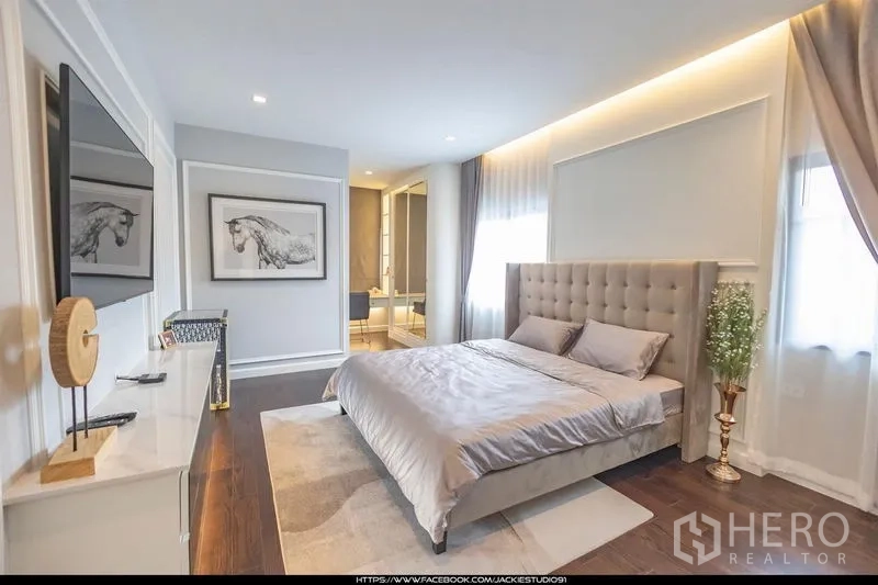 Detached House for sale in Pak Kret, Nonthaburi - Sunny guest bedroom with upholstered bed, TV wall and access to an ensuite bathroom.