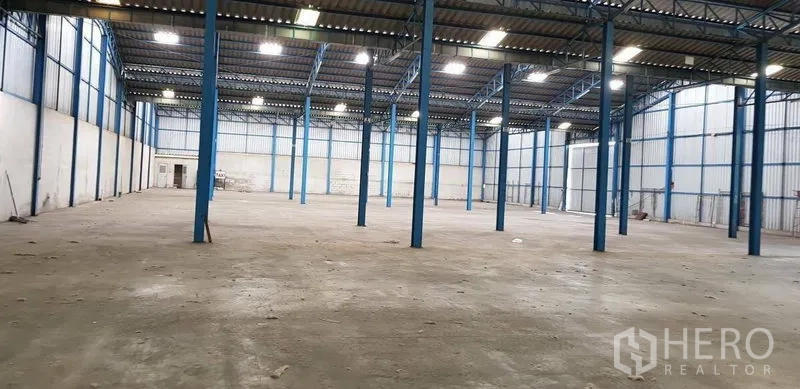 Warehouse for rent in Samut Prakan - Spacious warehouse interior with high steel columns, concrete floor and bright skylights.