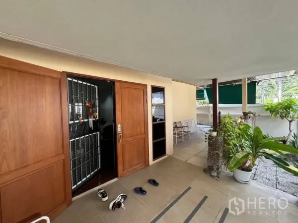 独立式住宅 出租在Watthana, Bangkok - 有顶门廊入口，木质大门与防盗门，摆放盆栽植物。