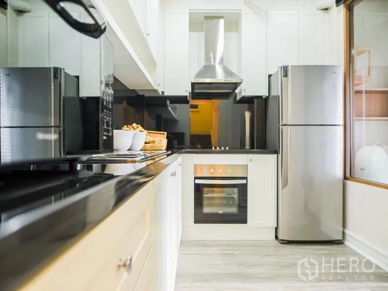 คอนโด ให้เช่าหรือขายในKhlong Toei, Bangkok - ครัวแบบแกลลอรี่ ตู้สีขาว ท็อปหินสีดำ เตาอบ เตาไฟฟ้า และตู้เย็นสแตนเลส