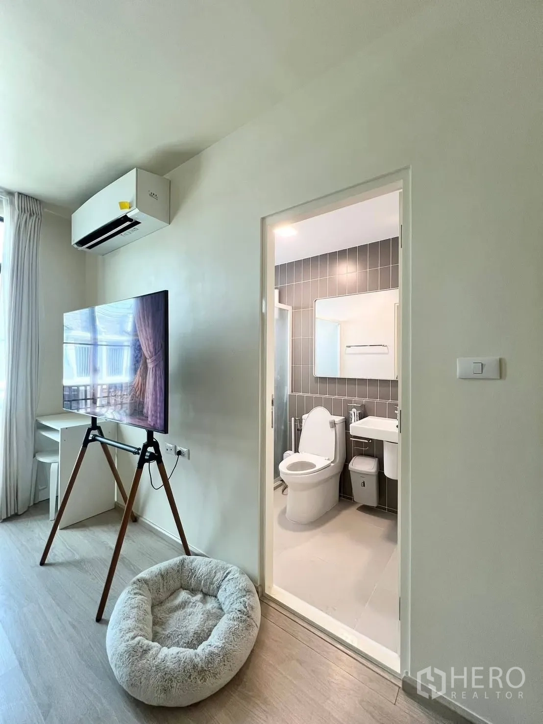 联排别墅 for rent in Bang Phli, Samut Prakan - 起居区连接浴室门，墙挂空调、落地支架电视与窗帘。