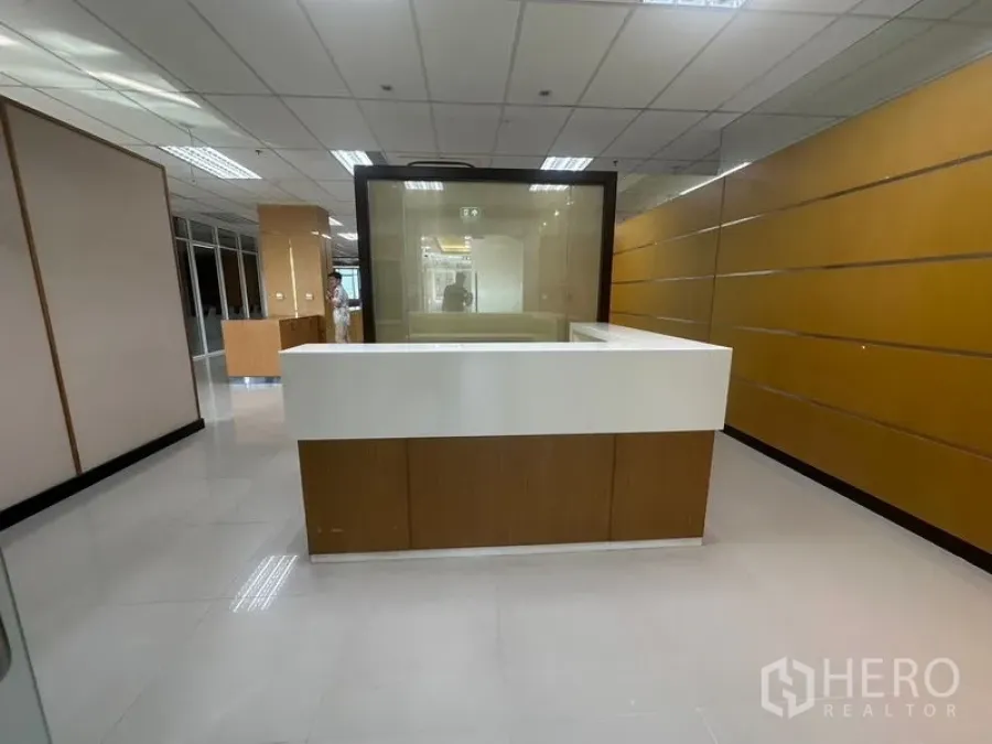 Office Space for rent in Suan Luang, Bangkok - Reception area with an L-shaped white desk and wood-paneled wall behind.