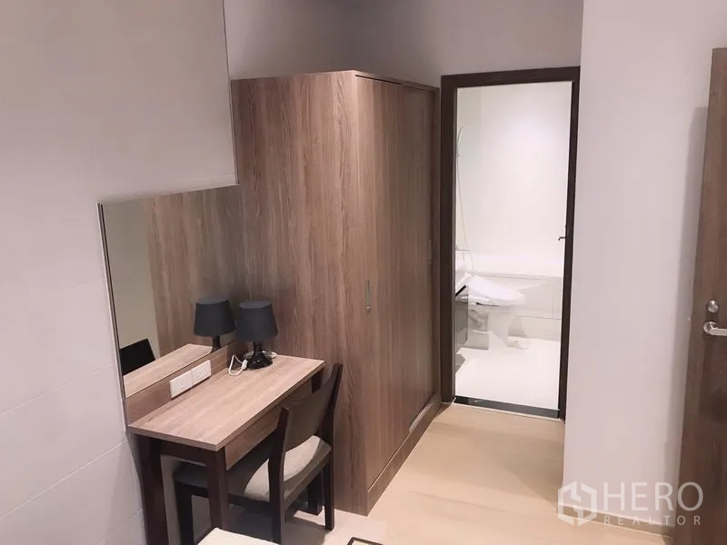 Condominium for rent or sale in Watthana, Bangkok - Compact dressing area with desk, mirror and wardrobe leading to a bright bathroom.