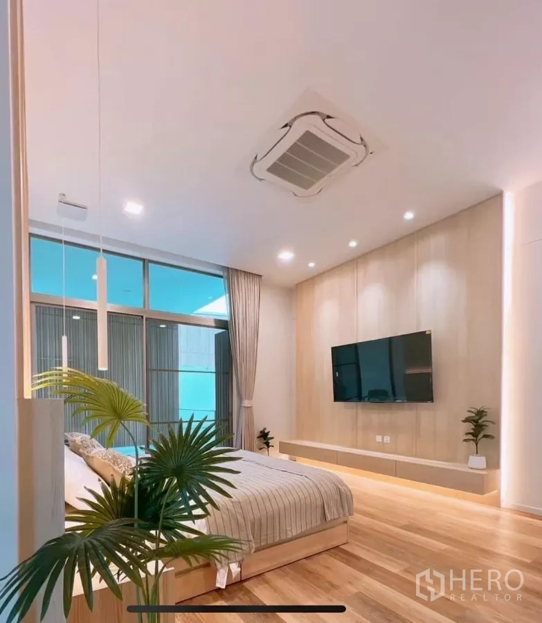 Detached House for rent in Saphan Sung, Bangkok - Primary bedroom with wall‑mounted TV, wood accent wall and sliding glass doors to a balcony.