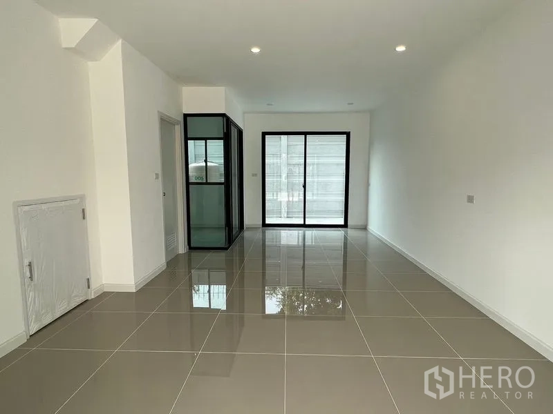 Townhouse for rent in Bang Kapi, Bangkok - Bright ground-floor living area with glossy tiles, recessed lighting and sliding glass doors.