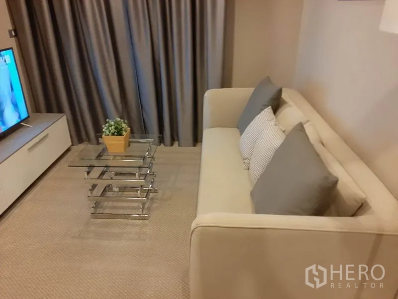 คอนโด ให้เช่าหรือขายในKhlong Toei, Bangkok - โซฟาพร้อมโต๊ะกลางกระจกแบบซ้อน ข้างชั้นวางทีวีและผ้าม่าน