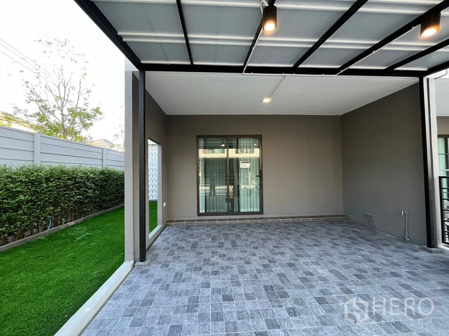 联排别墅 出租在Bang Phli, Samut Prakan - 带顶车棚，灰色地砖与吊灯，连接草坪和推拉玻璃门。