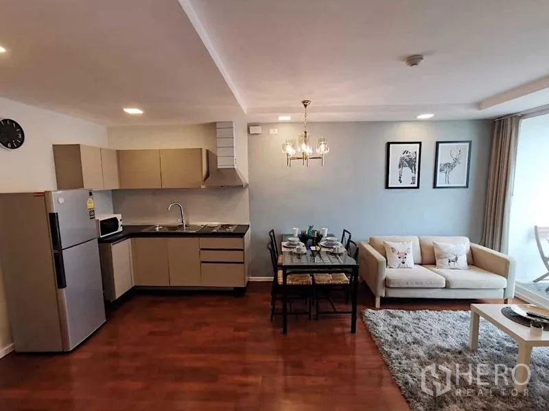 Condominium for sale in Khlong Toei, Bangkok - Open-plan living and dining with fitted kitchen, chandelier, sofa, and balcony doors.