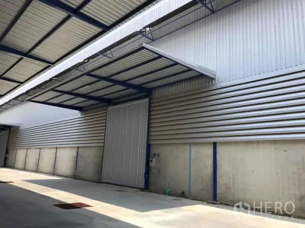 工厂 出租在Lat Lum Kaeo, Pathum Thani - 带雨棚的装卸区，配大型金属推拉门与混凝土车道的现代工厂外观。