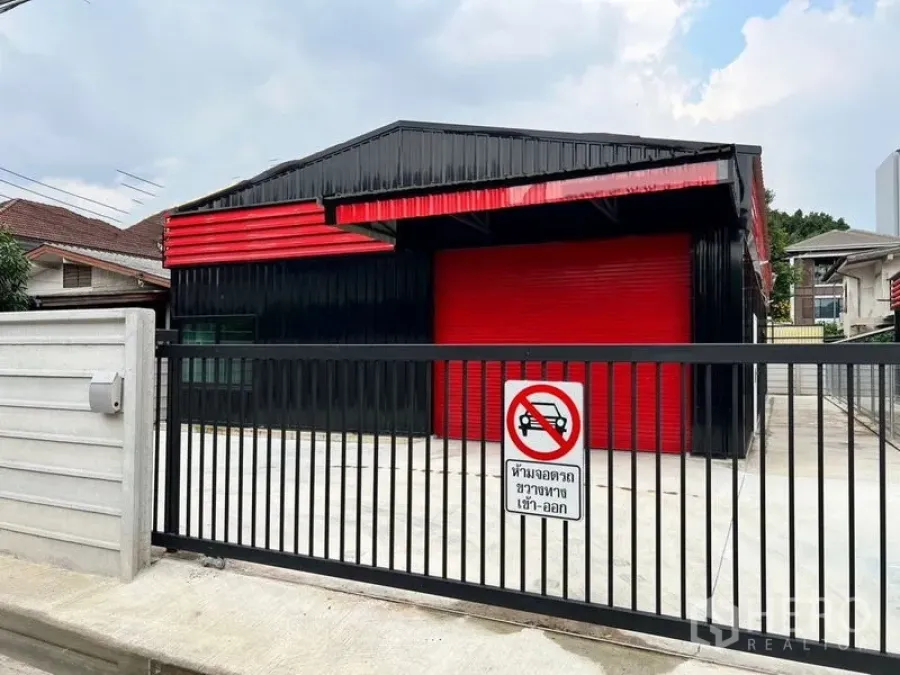 คลังสินค้า ให้เช่าในLat Phrao, Bangkok - ภายนอกโกดังสีดำแดง ประตูม้วนสีแดง พร้อมรั้วและลานคอนกรีตด้านหน้า