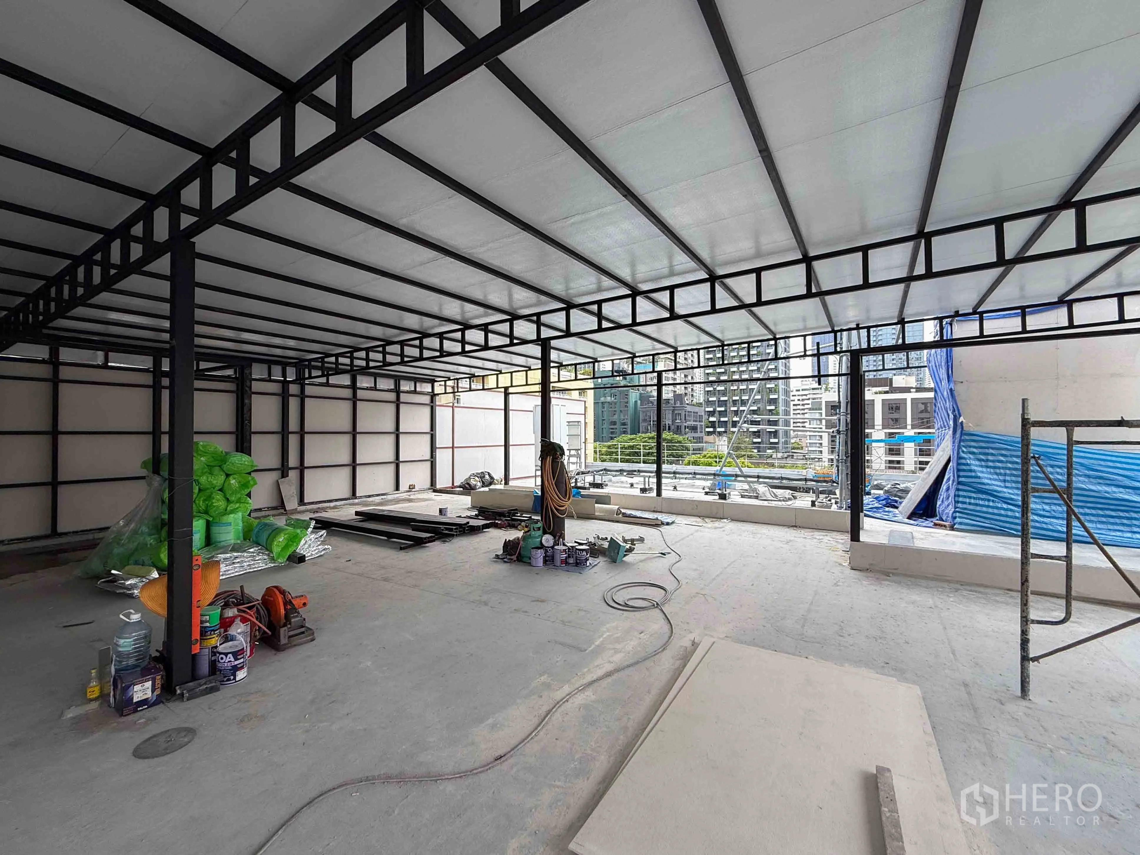Retail Space for rent in Watthana, Bangkok - Open shell space with metal beams and materials on the floor overlooking city buildings.