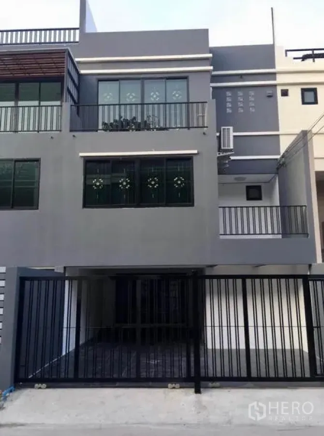 Townhouse for rent in Wang Thonglang, Bangkok - Modern three-storey grey townhouse facade with balconies and gated carport.