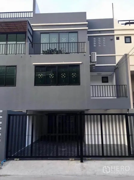 Townhouse for rent in Wang Thonglang, Bangkok - Modern three-storey grey townhouse facade with balconies and gated carport.