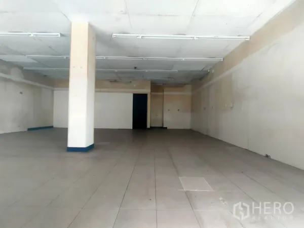 零售空间 出租在Khlong Toei, Bangkok - 开放式商铺内部，瓷砖地面、日光灯照明和中央立柱。