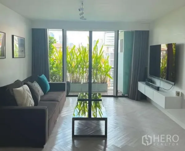 คอนโด ให้เช่าในKhlong Toei, Bangkok - พื้นที่นั่งเล่นมีประตูบานเลื่อนขนาดใหญ่สู่ระเบียงเขียวชอุ่มและทีวีติดผนัง