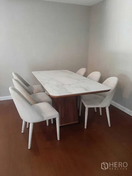 Condominium for rent or sale in Huai Khwang, Bangkok - Dining area with a marble-top table and six upholstered chairs on wood flooring.