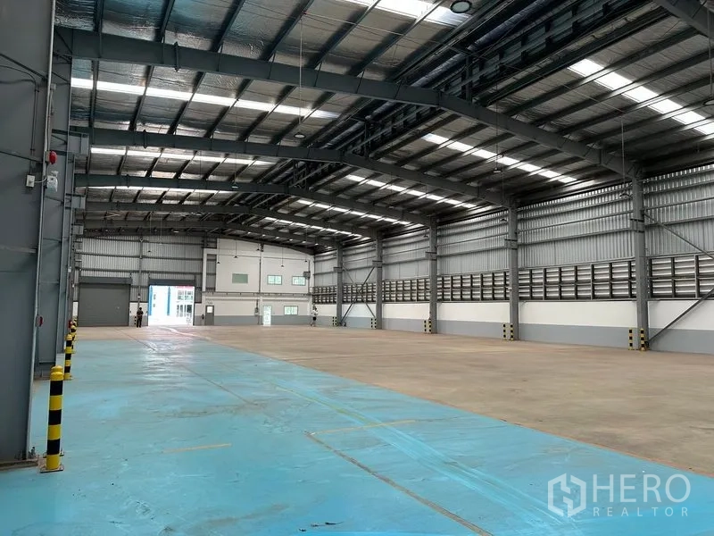 โรงงาน ให้เช่าในMueang Samut Prakan, Samut Prakan - ภาพกว้างของโกดัง แสดงโซนพื้นอีพ็อกซี่สีฟ้าและโครงสร้างเหล็กแข็งแรง