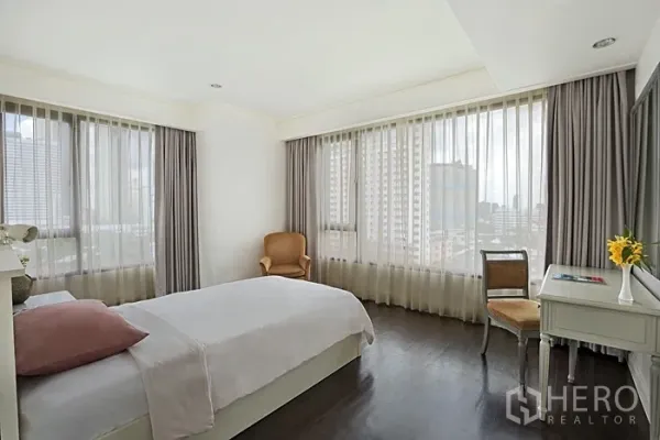 Condominium for rent in Khlong San, Bangkok - Corner bedroom with wraparound windows, city skyline views and a vanity desk.