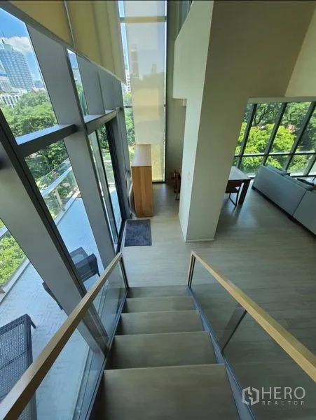 Condominium for rent or sale in Watthana, Bangkok - Duplex staircase next to double-height glass wall leading to a balcony with city and treetop views near Asok.