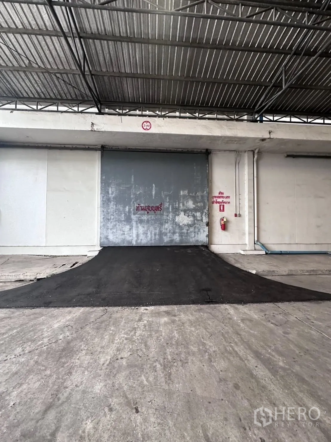คลังสินค้า for rent in Mueang Samut Prakan, Samut Prakan - ทางลาดขนถ่ายเข้าสู่ประตูม้วนสีเทาภายใต้กันสาดโลหะ