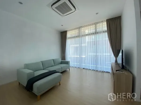 Townhouse for rent in Saphan Sung, Bangkok - Airy living room with large windows, cassette air-conditioner, sofa and media console.