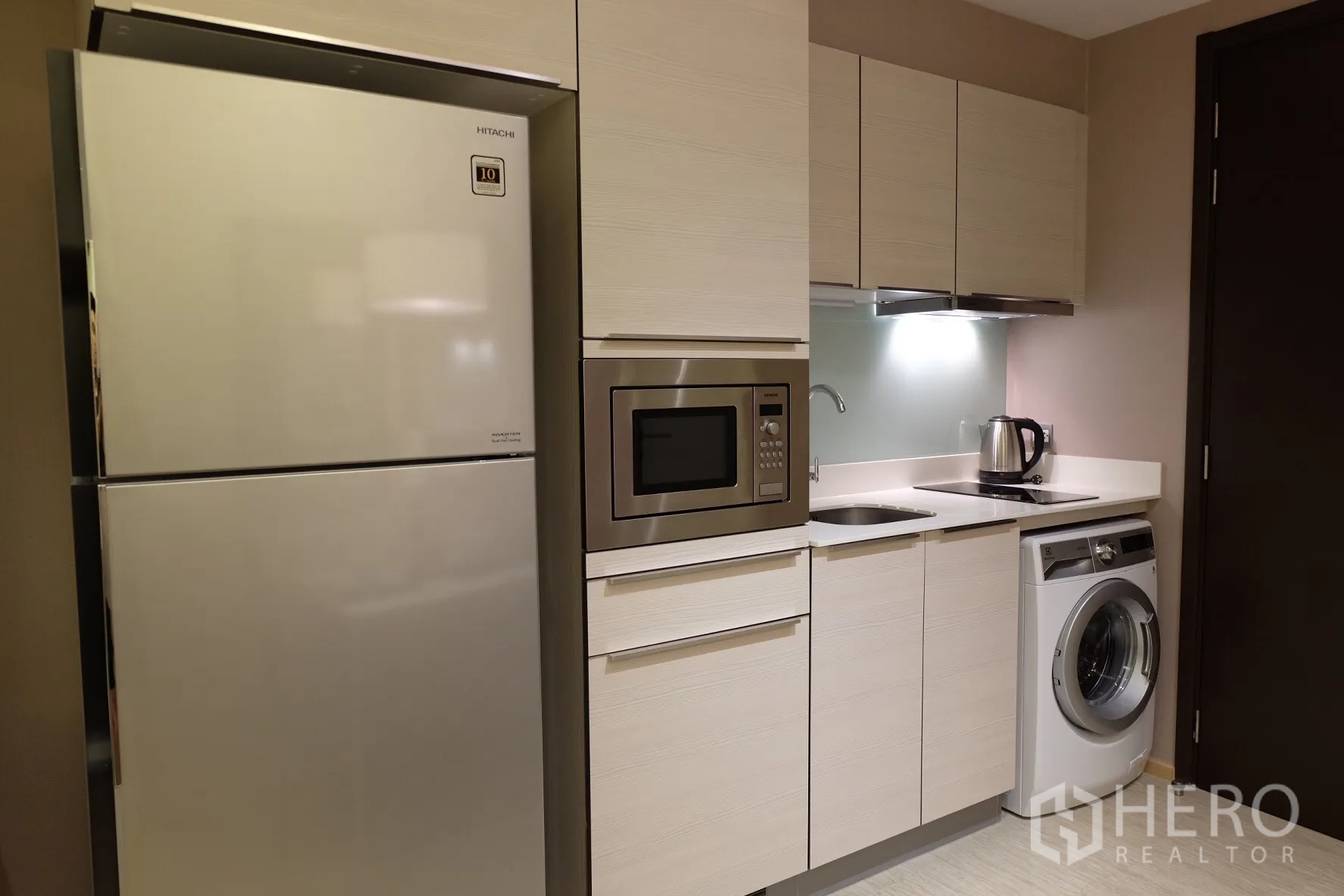 Condominium for rent in Watthana, Bangkok - Compact kitchenette with full-size refrigerator, built-in microwave, electric cooktop, sink and front-load washing machine.