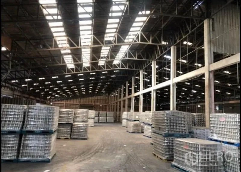 Factory for rent in Bang Khla, Chachoengsao - Expansive warehouse floor with skylights and neatly stacked palletised goods.