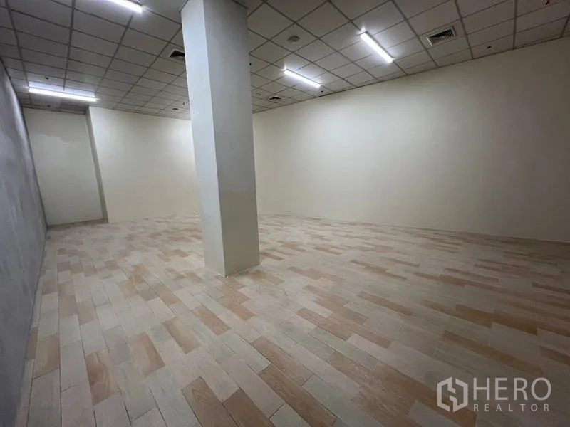 零售空间 出租在Watthana, Bangkok - 纵深视角的空铺，中央立柱、瓷砖地面与白色墙面。