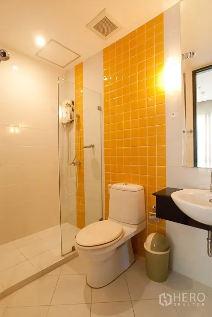 公寓 出租在Khlong Toei, Bangkok - 第二间浴室，黄色瓷砖点缀，玻璃淋浴间与白色洁具。