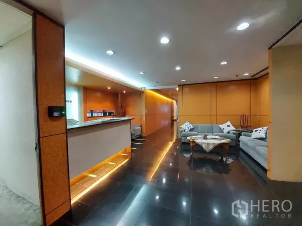 สำนักงาน ให้เช่าในRatchathewi, Bangkok - ล็อบบี้สำนักงานพร้อมเคาน์เตอร์ต้อนรับ ไฟแสงสว่าง ผนังลายไม้ โซฟาสีเทา และพื้นกระเบื้องดำเงา