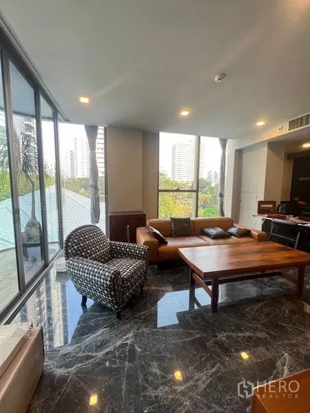 คอนโด ให้เช่าในWatthana, Bangkok - มุมห้องนั่งเล่นมองเห็นต้นไม้และอาคารเมือง พร้อมโซฟาหนังและพื้นหินอ่อน