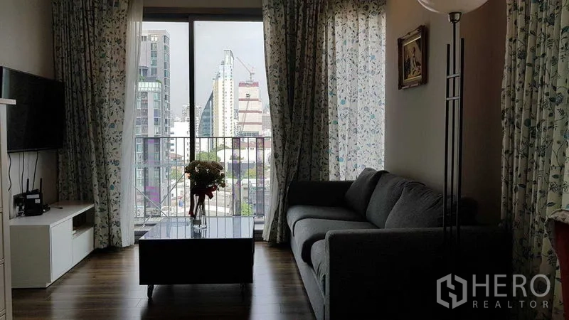 คอนโด ขายในWatthana, Bangkok - ห้องนั่งเล่นโซฟาสีเทา โต๊ะกลาง และประตูระเบียงเปิดรับวิวเมือง