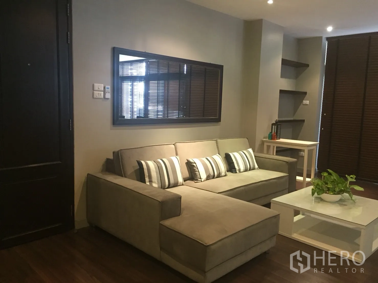 อพาร์ทเมนท์ ให้เช่าในKhlong Toei, Bangkok - ห้องนั่งเล่นโทนอบอุ่น โซฟาเข้ามุม หมอนลายทาง กระจกเงาบนผนัง และโต๊ะกลางสีขาว