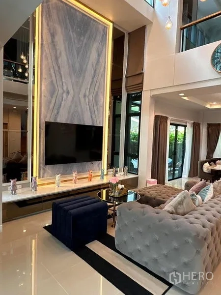 独立式住宅 出租在Prawet, Bangkok - 双层挑高客厅，大理石电视背景墙、纽扣绗缝沙发与大窗户。