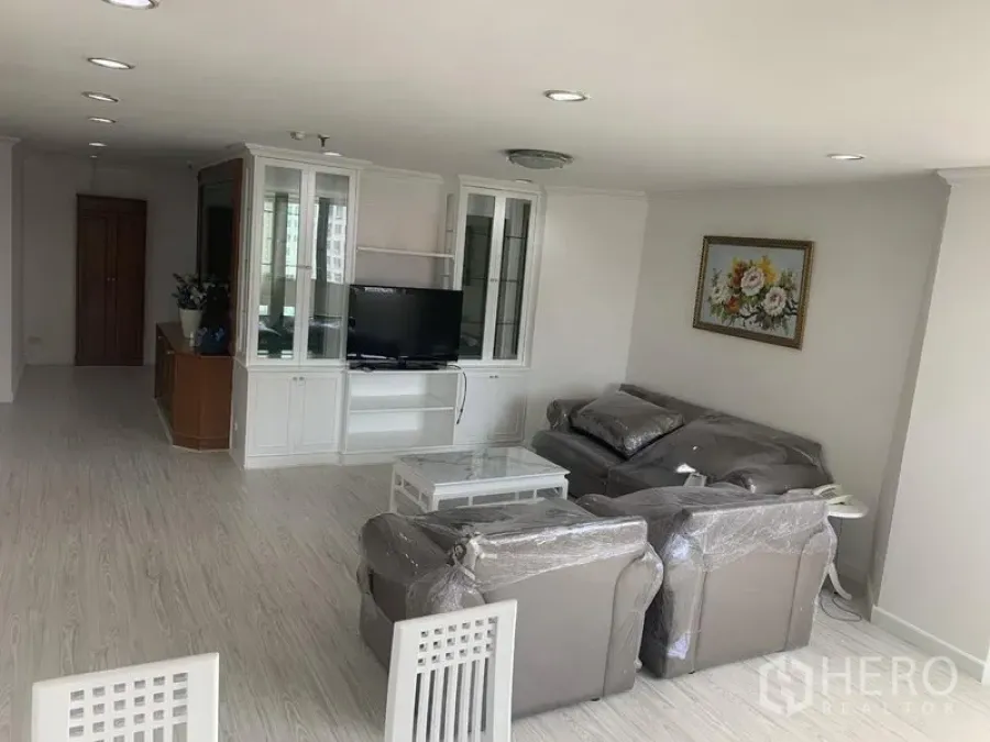 Condominium for rent in Watthana, Bangkok - Bright open-plan living room with gray sofa set, white built-in TV cabinet, light wood flooring and recessed lights.