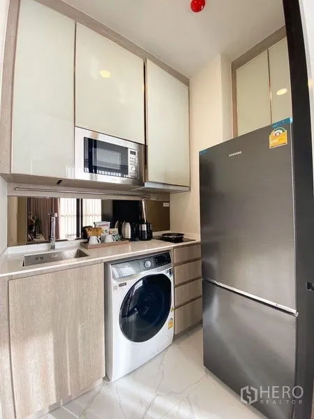 Condominium for rent in Ratchathewi, Bangkok - Kitchen view with tall stainless refrigerator, built-in microwave, washer and stone countertop.
