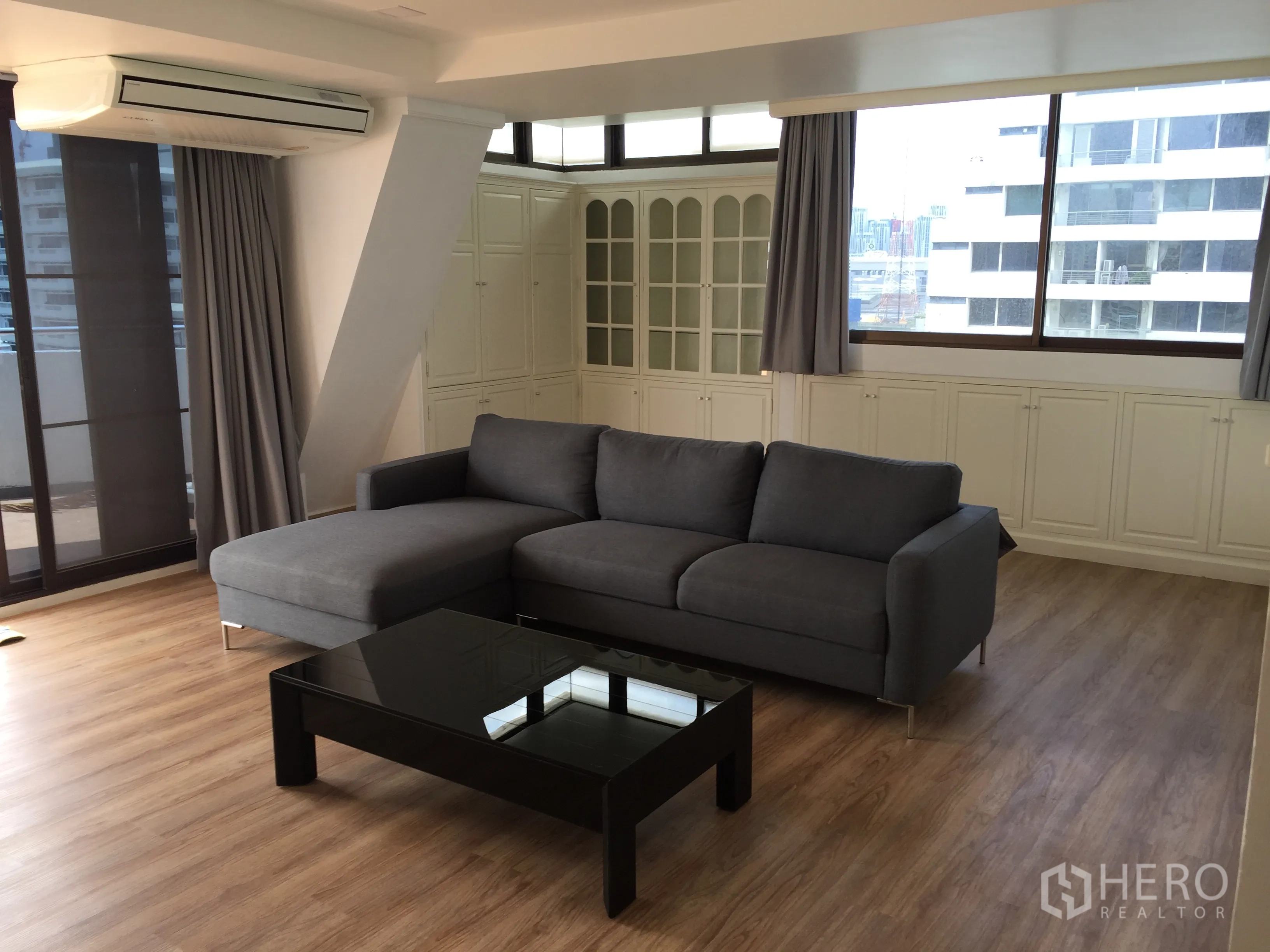 公寓 出售在Watthana, Bangkok - 客厅宽敞，灰色转角沙发，大窗与入墙收纳，连通阳台