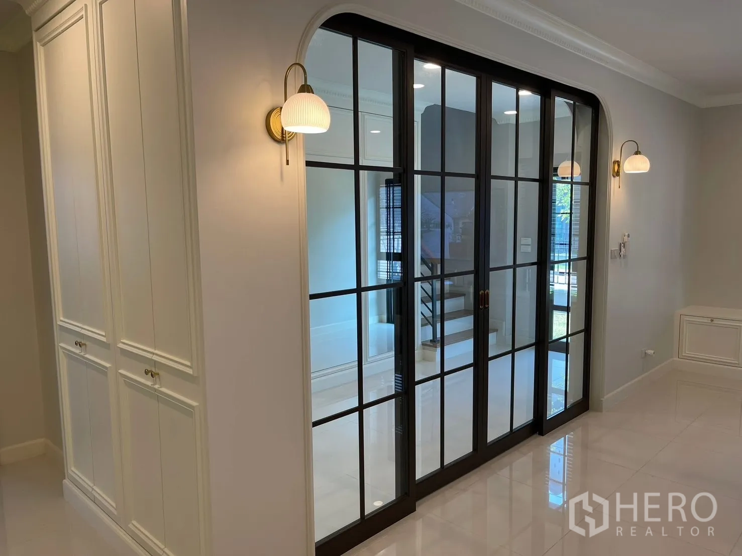 Detached House for rent in Bang Phli, Samut Prakan - Hallway detail showing black-framed sliding glass doors, wall sconces, and built-in cabinetry.