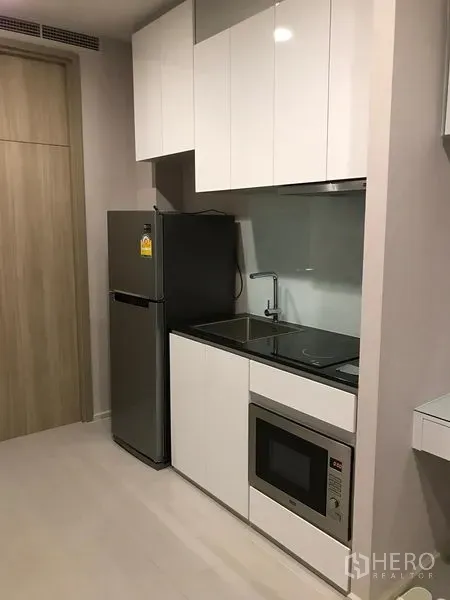 Condominium for rent in Pathum Wan, Bangkok - Compact modern kitchenette with white cabinets, stovetop, microwave and fridge