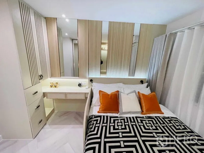 Condominium for sale in Yan Nawa, Bangkok - Close-up view of bed with orange pillows and backlit headboard beside vanity.