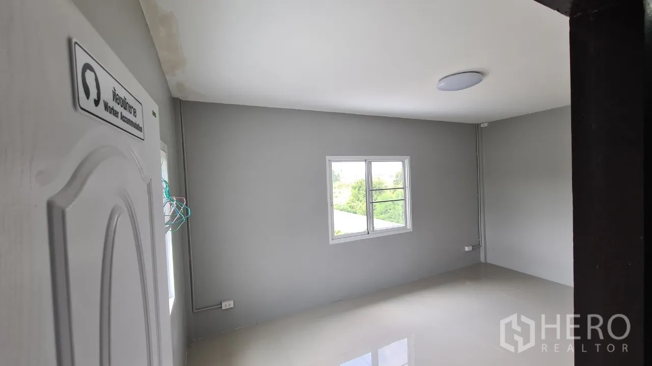Home Office for rent in Pathum Thani - Simple staff accommodation room with window views and light grey walls.
