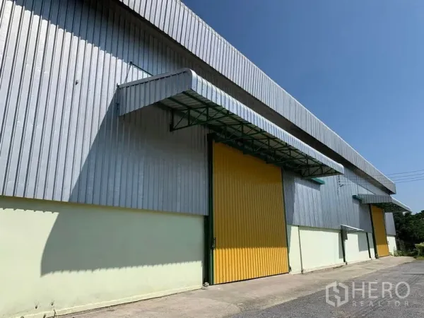 Warehouse for rent in Lat Krabang, Bangkok - Street-side view of a metal-sheet warehouse with an oversized yellow sliding door and shade canopy.