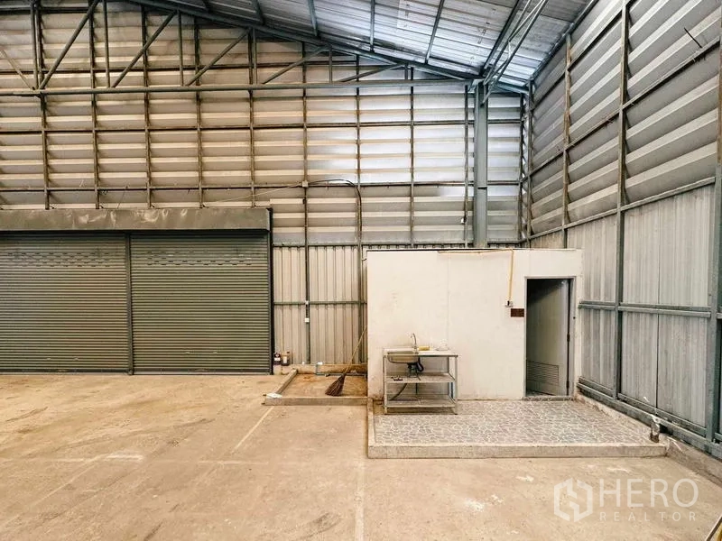 Warehouse for rent in Din Daeng, Bangkok - Corner of warehouse showing roller doors and a small utility room.