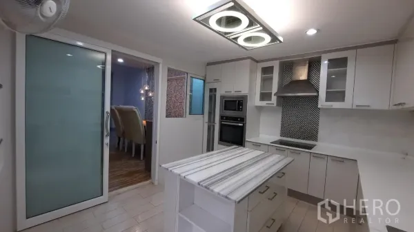 Townhouse for sale in Suan Luang, Bangkok - Modern white kitchen with island, built-in oven and glass sliding door