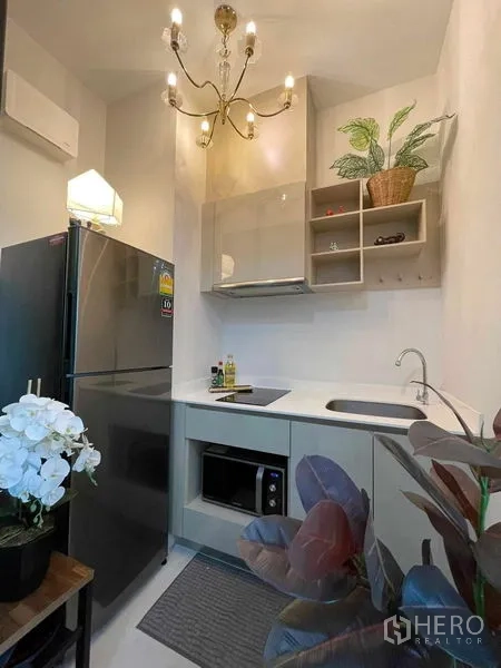 Condominium for sale in Huai Khwang, Bangkok - Compact kitchen with chandelier lighting, stainless refrigerator, built-in cabinets, sink and microwave.